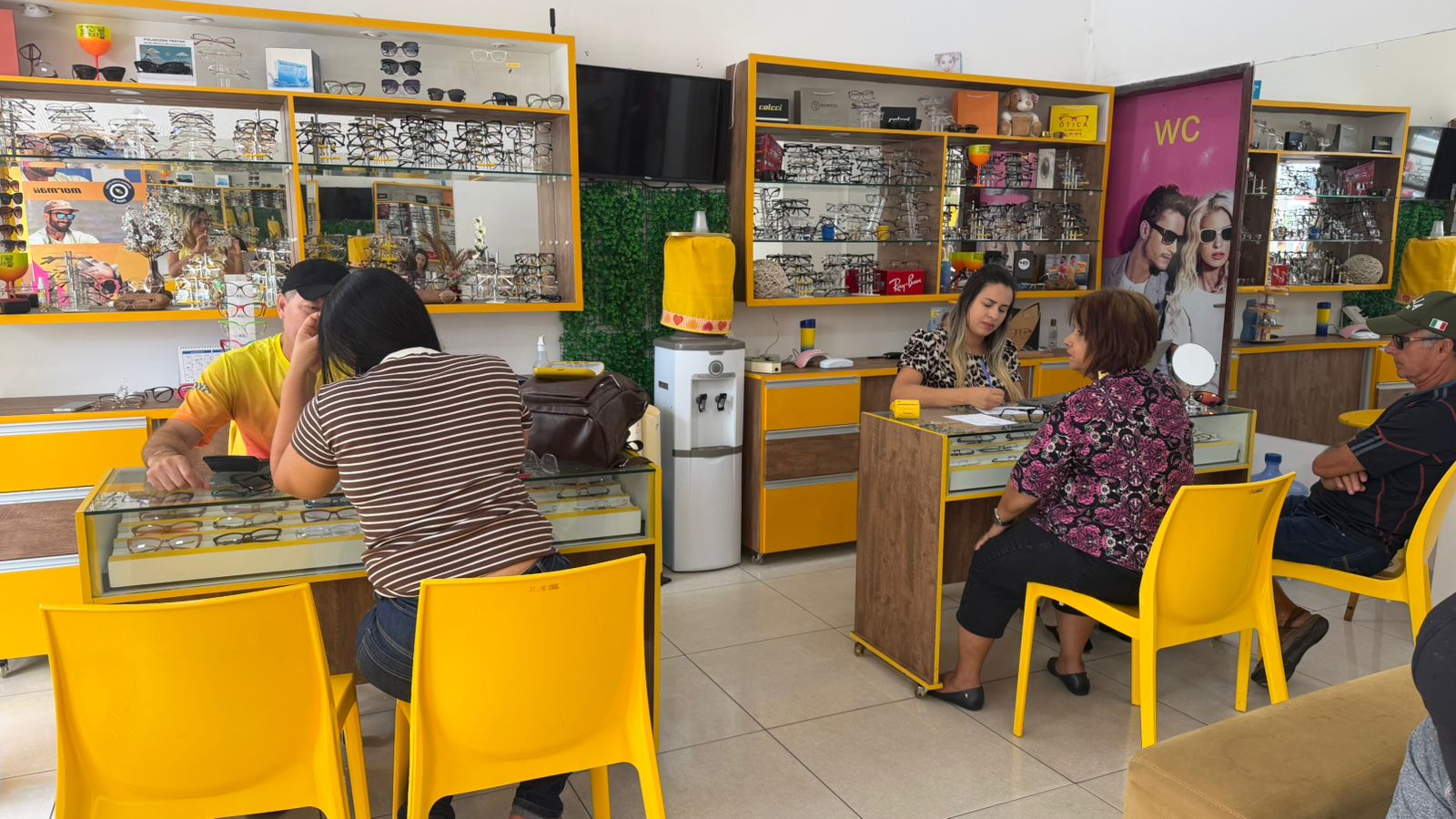 Interior da loja Cleber Ótica com clientes sendo atendidos